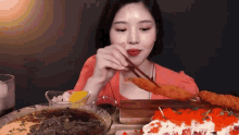 a woman is eating food with chopsticks and a plate of food in the background .