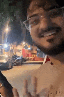 a man with glasses and a beard is smiling while standing on a street .