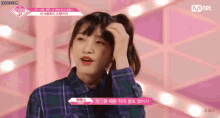 a girl in a plaid shirt is holding her hair in a ponytail in front of a mnet logo