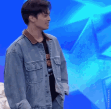 a young man wearing a denim jacket is standing in front of a blue background