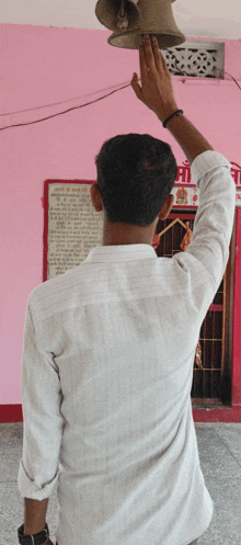 a man in a white shirt holds up his hand to a bell