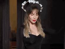 a woman wearing a black dress and a crown of flowers on her head is standing in a doorway .