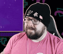 a man with a beard wearing glasses and a beanie is sitting in front of a computer screen .