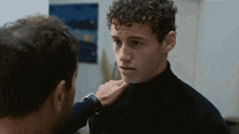 a man with curly hair is talking to another man with a watch on his wrist