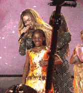 a woman is singing into a microphone while standing next to a little girl in a gold dress .