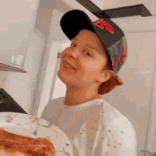 a person wearing a baseball cap is holding a plate of pizza .