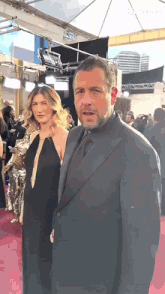 a man in a suit and tie stands next to a woman on a red carpet