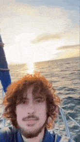 a man with curly hair and a beard is on a boat in the ocean .