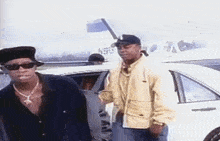 a man in a yellow jacket is standing next to a man in a black shirt and sunglasses