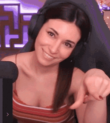 a woman wearing headphones and a striped tank top is pointing at the camera