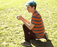 a boy with blue hair is squatting down in the grass