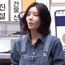 a woman wearing overalls stands in front of a sign that says ' korean '