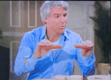 a man in a blue shirt is sitting at a table eating a hot dog