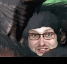a man wearing glasses and a black hat is sitting in a pile of people .