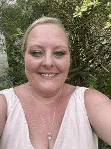 a woman wearing a necklace and earrings smiles in front of a bush