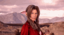 a woman in a red jacket is standing in a desert looking at the camera .