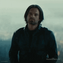 a man with long hair and a beard is wearing a black leather jacket and looking at the camera .
