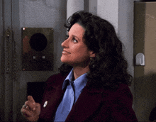 a woman in a blue shirt and a burgundy jacket stands in front of a door