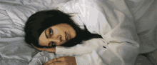 a woman in a white shirt is laying on a bed with her head on her hand
