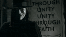 a person wearing a mask and a hat stands in front of a sign that says through unity through faith
