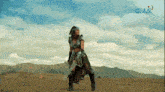 a woman in a warrior costume is dancing in the desert in front of a gma sign