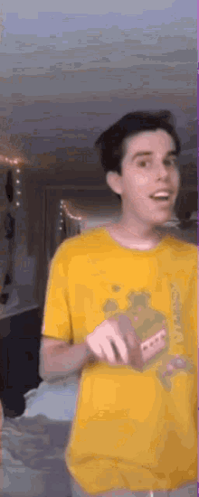 a young man in a yellow shirt is standing in a room and smiling .