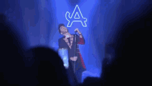 a man is singing into a microphone on stage in front of a neon sign that says a .