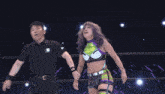 a female wrestler with purple hair and a green top holds her arms up in the air