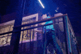 a man is standing on a balcony at night with a blue light behind him .