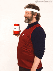 a man wearing a red vest and a white headband is holding a can that says utility