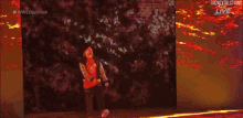 a man in a red shirt is dancing on a stage in front of a wall that says wwe backlash live .