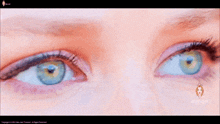 a close up of a woman 's blue eyes with a lion logo on the bottom of the screen