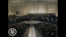 a man stands on a stage in front of a crowd and a sign that says tech 80