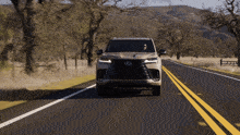 a lexus suv is driving down a road with mountains in the background