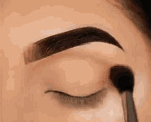 a close up of a woman applying eye shadow to her eyebrows with a brush .