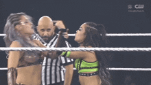 two women are wrestling in a ring while a referee looks on and a cw logo is visible in the background