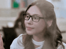 a woman wearing glasses and a white shirt looks at something