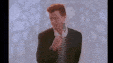 a man in a suit and tie is singing into a microphone in front of a white wall .