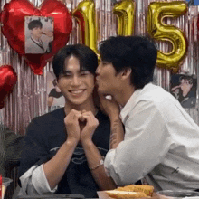 a man is kissing another man on the cheek in front of balloons with the number 15 on them