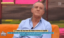 a man in a blue shirt is sitting on an orange couch on a television show