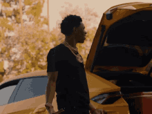 a man in a black shirt stands next to a yellow car with the trunk open