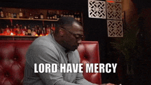 a man sitting on a red couch with the words lord have mercy written above him