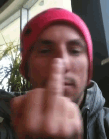 a man wearing a pink hat and a grey jacket is giving the middle finger