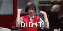 a woman in a red vest is flexing her muscles in a store and saying `` i did it ! ''