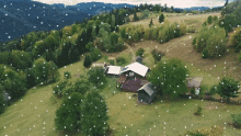 snow is falling on a lush green hillside with a house in the middle