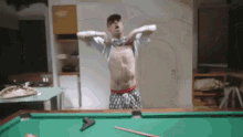 a shirtless man is standing on a pool table