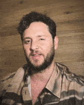 a man with a beard wearing a plaid shirt looks at the camera