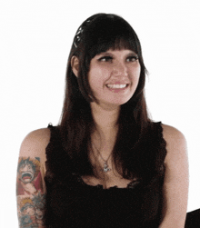 a woman with a tattoo on her arm is wearing a black tank top and smiling .