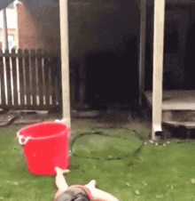 a person laying on the grass with a red bucket in the foreground