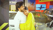 a man in a white shirt is hugging a woman in a yellow saree in a parking lot